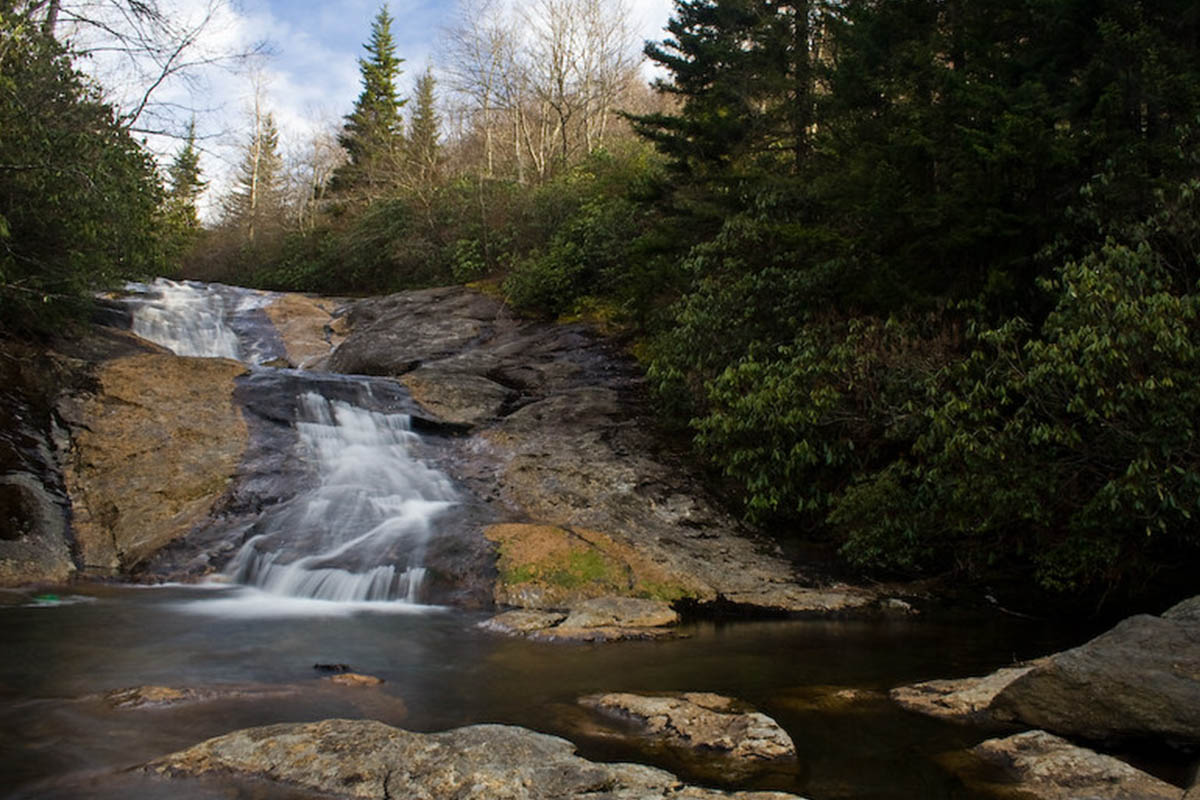 Cascading waterfall flowing over smooth rock into a forest pool along the Blue Ridge Parkway