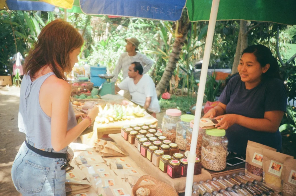 Person shopping at an outdoor farmers market with a local vendor selling handmade goods
