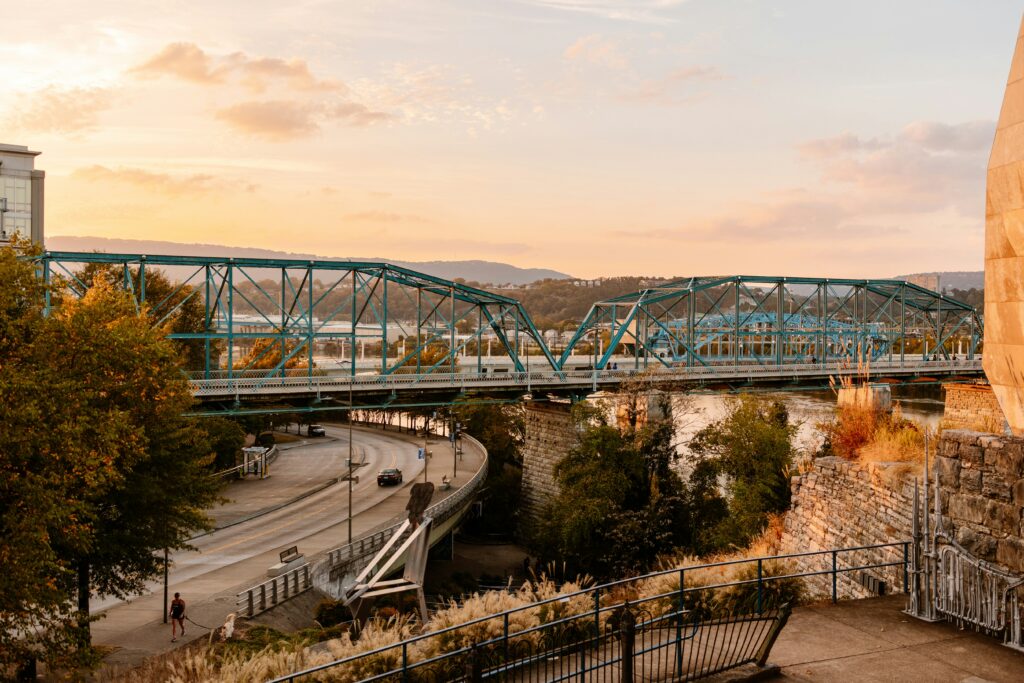 Walnut Street Bridge in Chattanooga, Tennessee at sunset, spanning the Tennessee River with downtown and Lookout Mountain in the background.