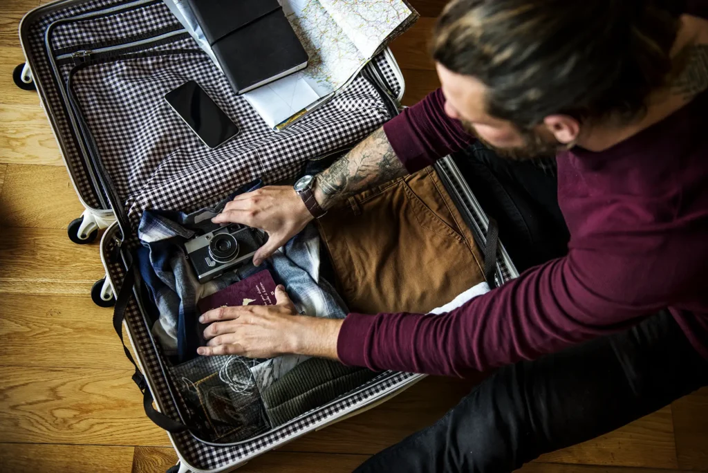 Man packing a suitcase with clothes, camera, passport, and travel essentials