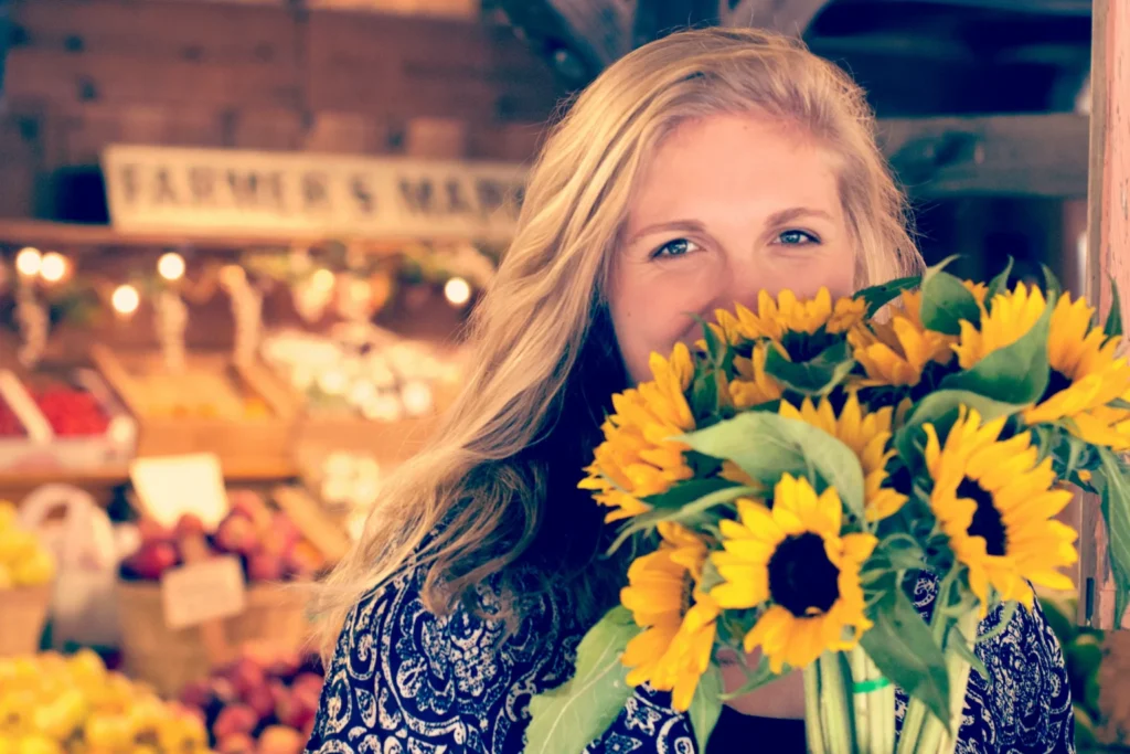 A smiling woman holding up a bouquet of sunflowers in front of her